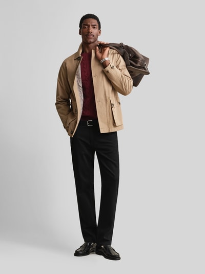 Männermodel trägt Regular Fit Pullover aus reiner Baumwolle von GANT in Dunkelrot, kombiniert mit schwarzer Hose, Ganzkörperansicht von vorne.