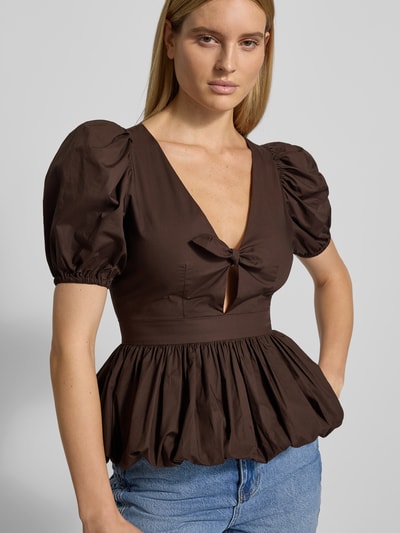 Frauenmodel trägt Blusenshirt mit V-Ausschnitt von ROTATE aus reine Baumwolle, lockerer Schnitt, Schleifen-Detail, Nahaufnahme Oberkörper.