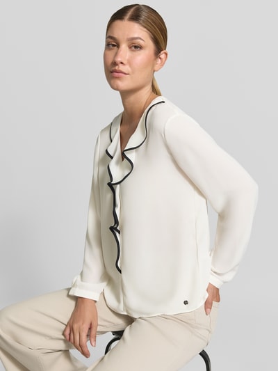 Frauenmodel trägt Regular Fit Bluse mit Volants von Marc Cain in Offwhite mit schwarzem Saum, V-Ausschnitt, Label-Detail, Nahaufnahme Oberkörper.