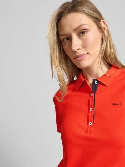 Frauenmodel trägt Slim Fit Poloshirt mit Label-Stitching von Gant aus Baumwoll-Elasthan-Mix, Knopfleiste, Rückenlänge 59 cm bei Größe S, Nahaufnahme Oberkörper.