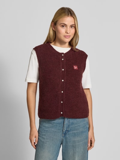 Kobiece model prezentuje Regular Fit Weste mit Alpaka-Woll-Anteil von American Vintage, elastyczna mieszanka materiałów, imitacja dzianiny, detal z logo, listwa guzikowa, długość tyłu w rozmiarze S: 53 cm, widok całej sylwetki z przodu.