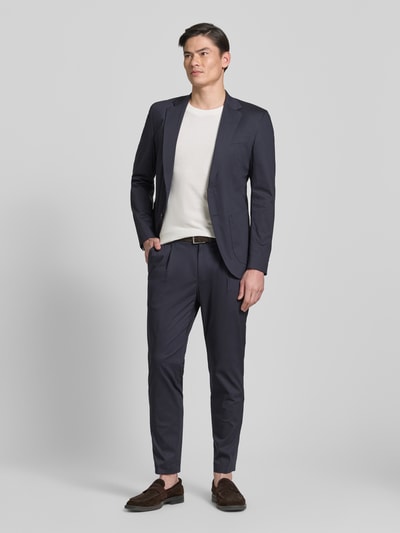 Männermodel trägt Regular Fit Stoffhose mit Logo-Detail Modell 'Lester' von JOOP! Collection, dunkelblau, Baumwoll-Mix, Bundfalten, Gesäßtaschen, Knopf- und Reißverschluss, Ganzkörperansicht von vorne.