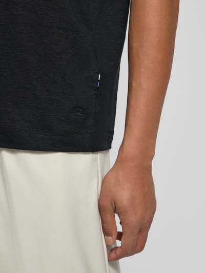 Männermodel trägt schwarzes Slim Fit Poloshirt aus Leinen-Elasthan-Mix von OLYMP Level Five, Halbarm, Detailaufnahme seitlich.