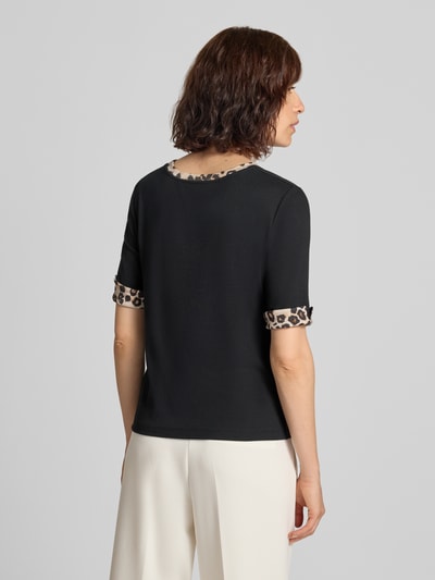 Frauenmodel trägt Regular Fit T-Shirt mit Animal-Print von Marc Cain, elastischer Baumwoll-Mix, Halbarm, schwarzer Grundton mit Animal-Print-Details an den Ärmeln und am Halsausschnitt, Rückenlänge 55 cm, Ganzkörperansicht Rückansicht.