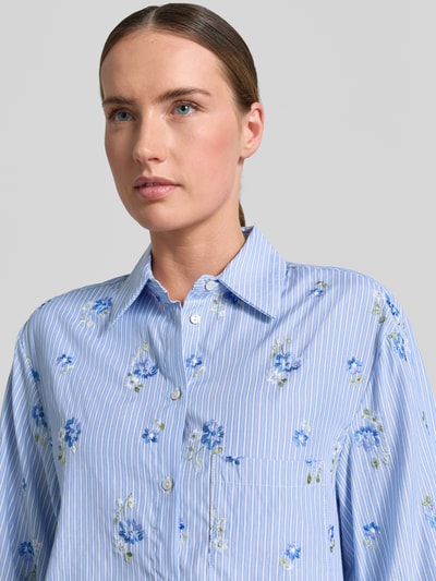 Frauenmodel trägt Damen Hemdbluse mit Knopfleiste Modell 'FLORIX' von Mango, Material-Mix mit Viskose-Anteil, Regular-Fit, Hemdblusenkragen, dezentes Streifenmuster mit blauen Blumen-Muster, Nahaufnahme Oberkörper.