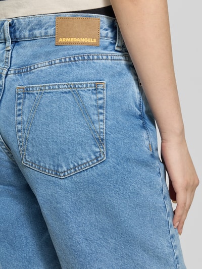 Frauenmodel trägt Regular Fit Jeansshorts aus reiner Baumwolle Modell 'THALINAA' von Armedangels, blaue Twill-Textur, Label Patch, 5-Pocket-Design, Logo-Prägung, Nahaufnahme Rückansicht.