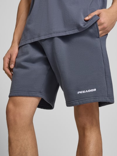 Männermodel trägt Shorts mit elastischem Bund und Logo-Stitching von Pegador in Grau, Baumwoll-Mix, Loose-Fit, Nahaufnahme Oberschenkel.