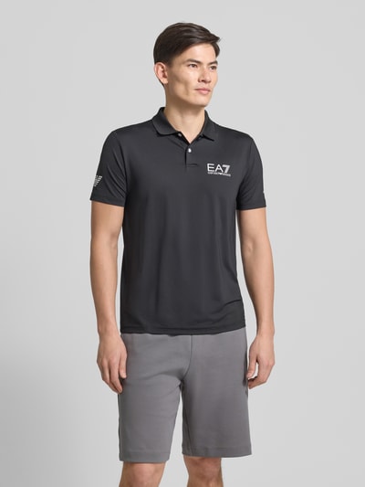 Männermodel trägt Regular Fit Poloshirt mit Logo von EA7 Emporio Armani, schwarzer Material-Mix mit Stretch-Anteil, Polokragen, Knopfleiste, Logo, Ganzkörperansicht von vorne.