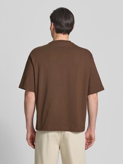 Männermodel trägt Relaxed Fit T-Shirt aus reiner Baumwolle Modell 'BOXYNORMAN GRAPHIC' von SELECTED HOMME in Braun, Ganzkörperansicht Rückansicht.