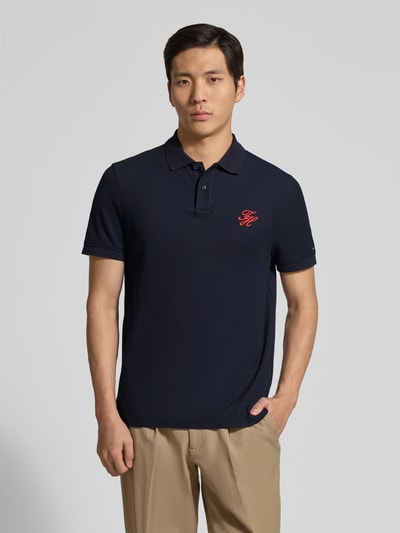 Männermodel trägt Regular Fit Poloshirt aus reiner Baumwolle von Tommy Hilfiger, Optik: Unifarben, Logo-Stitching, Polokragen, Kurzarm, Ärmelabschluss: Gerippt, Rumpfabschluss mit Seitenschlitzen, Materialverarbeitung: Piqué, Farbe dunkelblau, Ganzkörperansicht von vorne.