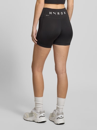 Frauenmodel trägt PUMA x HYROX - Shorts mit Label-Print in Schwarz, körpernaher Schnitt, elastischer Bund, Material-Mix mit Stretch, Ganzkörperansicht Rückansicht.
