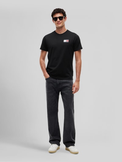 Männermodel trägt schwarzes Slim Fit T-Shirt aus reiner Baumwolle von Tommy Jeans, kombiniert mit dunkler Jeans, Ganzkörperansicht von vorne.