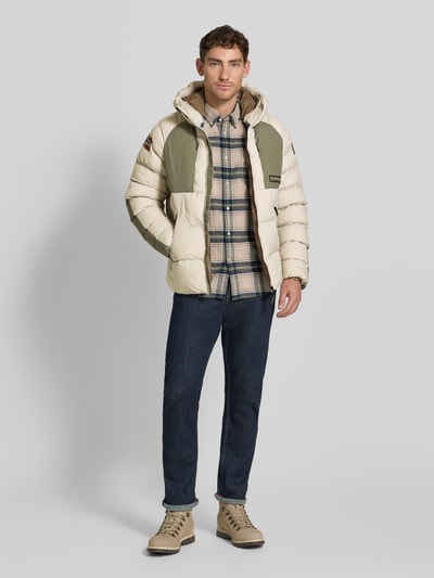 Männermodel trägt Regular Fit Steppjacke mit Logo-Patch Modell 'MOESA' von Napapijri in Beige und Oliv, Ganzkörperansicht von vorne, Herrenjacke mit Kapuze, Reißverschlusstaschen und gesteppten Flächen.