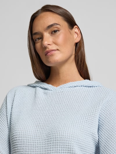 Frauenmodel trägt Strickshirt mit Kapuze Modell 'Gikaria' von OPUS in Hellblau, Strukturmuster, Material-Mix, Nahaufnahme Oberkörper.
