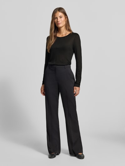 Frauenmodel trägt Longsleeve in semi-transparenter Optik von MYON, taillierter Schnitt, schwarzer Lyocell-Mix mit Woll-Anteil, Rundhalsausschnitt, Ziernaht, kombiniert mit dunkler Hose, Ganzkörperansicht von vorne.