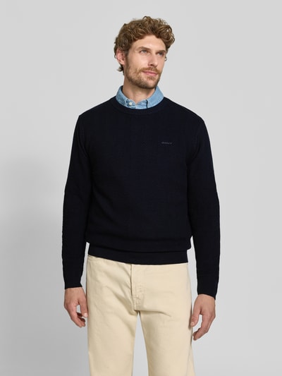 Männermodel trägt Regular Fit Pullover aus Baumwoll-Woll-Mix von GANT in Dunkelblau, helle Hose, Ganzkörperansicht von vorne.