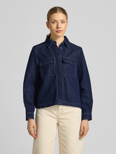 Modelka nosi Jeansbluse mit Brusttaschen und Kentkragen od Stefanel, ciemnoniebieski bawełniany krój regular fit z ukrytym zapięciem, sportowe mankiety, kieszenie na piersi z patkami, długość tyłu w rozmiarze S: 58 cm, długość rękawa: 55 cm, widok całej sylwetki z przodu.