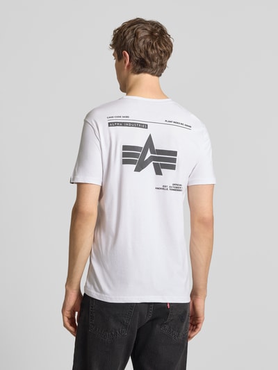 Männermodel trägt T-Shirt mit Label-Patch von Alpha Industries in Weiß, Reine Baumwolle, Gerader-Schnitt, Rückenlänge 66 cm, Ganzkörperansicht Rückansicht