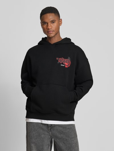 Männermodel trägt schwarzen Regular Fit Hoodie aus reiner Baumwolle Modell 'DAGETHOOD' von HUGO mit Motiv-Print und Kängurutasche, Optik: Unifarben, Sweat-Textur, Ganzkörperansicht von vorne.