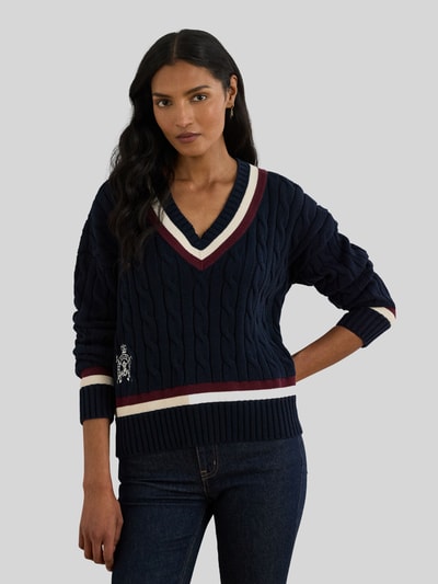 Frauenmodel trägt Regular Fit Strickpullover aus reiner Baumwolle von Lauren Ralph Lauren in Optik: Unifarben, Zopfmuster, Logo-Detail, gerippte Abschlüsse, Kontraststreifen, V-Ausschnitt, Langarm, Strick, Ganzkörperansicht von vorne.