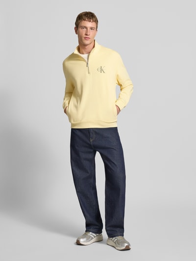 Männermodel trägt Sweatshirt mit Stehkragen und Reißverschluss von Calvin Klein Jeans in Hellgelb, Regular-Fit, reine Baumwolle, Logo, Ganzkörperansicht von vorne.