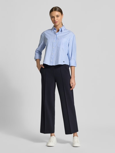 Modelka nosi Straight Fit Stoffhose mit Ziernaht Modell 'Cameron' od Cambio, ciemnogranatowy, elastyczny pas, widoczne kieszenie tylne, szerokość w rozmiarze 36: 39 cm, długość wewnętrzna nogawki w rozmiarze 36: 67 cm, skrócony fason, widoczny logo print, widok całej sylwetki z przodu