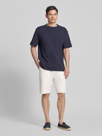 Männermodel trägt Relaxed Fit Bermudas aus Baumwoll-Mix Modell 'DETROIT' von s.Oliver RED LABEL in Beige mit Waffelstruktur, Ganzkörperansicht von vorne.