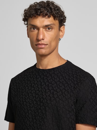 Männermodel trägt T-Shirt mit Logo-Muster und Rundhalsausschnitt von ARMANI EXCHANGE, zwarte katoen, slim fit, Nahaufnahme Oberkörper.