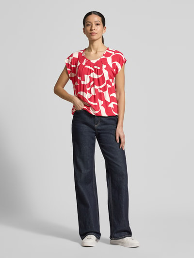 Vrouwenmodel draagt Regular Fit blouse uit viscosemix model 'Minou' van ZABAIONE met bloemen all-over print, korte mouw, ronde hals, elastische band, ruglengte maat S ca. 62 cm, kleurrijke rode en witte tinten, eenvoudige stofstructuur, geheel vooraanzicht.