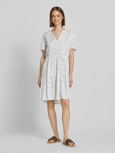 Frauenmodel trägt tailliertes Sommerkleid aus reiner Viskose Modell 'ZALLY LIFE' von Only mit Allover-Muster in Weiß und Blau, Mini-Länge, V-Ausschnitt, Kurzarm, Ganzkörperansicht von vorne.