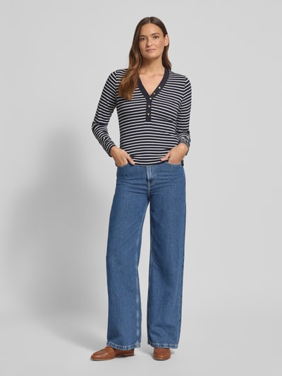 Modelka kobieca nosi Bluzka z długim rękawem Regular Fit Longsleeve mit Rüschenbesatz von zero z elastycznej mieszanki bawełny, krój regular fit, obszycie falbanami, ozdobne obszycie, dekolt w serek, długość tyłu w rozmiarze 36: 54 cm, granatowe i białe pasy, szerokie niebieskie spodnie, brązowe buty, widok całej sylwetki z przodu.