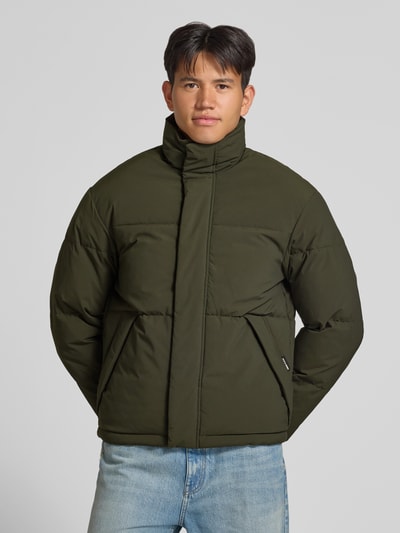 Männermodel trägt Steppjacke mit verdecktem Reißverschluss Modell 'SOHO' von JACK & JONES in Olivgrün, glatte Oberfläche, Ganzkörperansicht von vorne. Herren Steppjacke, Regular Fit, Stehkragen, Rückenlänge 70 cm, Schulterbreite 47 cm, Brustweite 60 cm, Ärmellänge 68 cm.