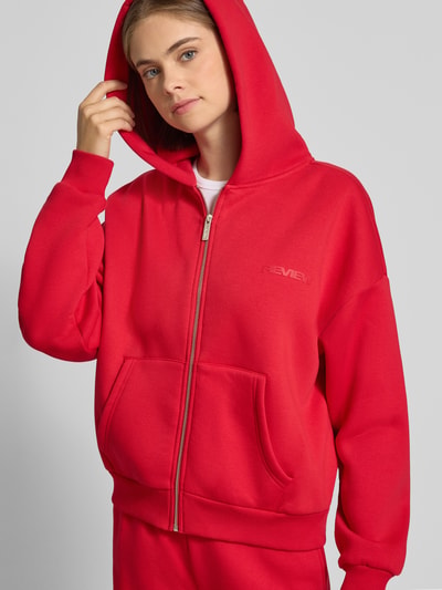 Frauenmodel trägt Relaxed Fit Basic Sweatjacke mit Kapuze von REVIEW, Baumwoll-Mix, Logo-Print, Kängurutasche, Ganzkörperansicht von vorne.