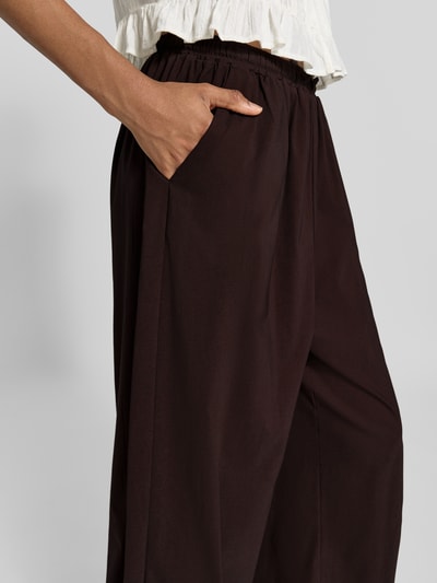 Frauenmodel trägt Balloon Fit Stoffhose aus Viskose-Mix Modell 'Hamy' von FREE/QUENT in Dunkelbraun, sichtbarer elastischer Bund, Eingrifftasche, Nahaufnahme Oberkörper. Damen Stoffhose, Viskose-Elasthan-Mix, elastische Beinabschlüsse, Bundweite S: 37 cm, Innenbeinlänge S: 74 cm.