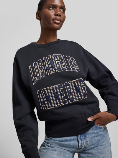 Frauenmodel trägt Sweatshirt aus reiner Baumwolle von Anine Bing, lockere Passform, Rundhalsausschnitt, Label-Detail, elastische Abschlüsse, dunkle Farbe, Rückenlänge bei Größe S 58 cm, Ganzkörperansicht von vorne.