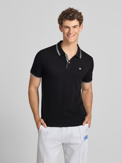 Männermodel trägt Slim Fit Poloshirt mit Label-Stitching von CHAMPION in Schwarz, reine Baumwolle, Knopfleiste, Ganzkörperansicht von vorne.
