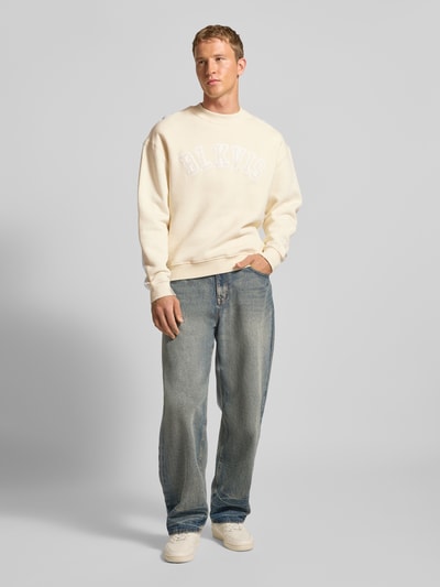 Männermodel trägt Sweatshirt mit Logo und Rundhalsausschnitt von BLKVIS aus reiner Baumwolle im Relaxed-Fit, cremefarben, Ganzkörperansicht von vorne.