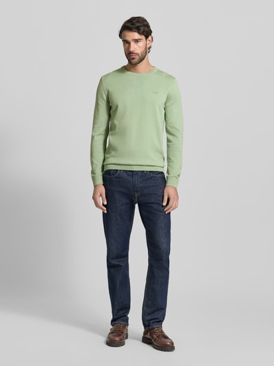 Męski model nosi Regular Fit Pullover aus reiner Baumwolle od s.Oliver RED LABEL, jasny zielony melanż, krój regular fit, okrągły dekolt, długi rękaw, ściągacze, gładka faktura dzianiny, widoczne label stitching, widok całej sylwetki z przodu.