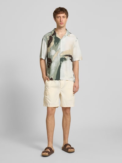 Męski model nosi Relaxed Fit Freizeithemd aus Viskose-Leinen-Mix Modell 'HARVI' von Only & Sons, efekt: wzór na całej powierzchni, krój relaxed fit, kołnierzyk koszulowy, listwa guzikowa na całej długości, krótki rękaw, cieniowana przędza, materiał: mieszanka wiskozy i lnu, jasne beże, zielenie i ciemne brązy, tekstura lekko matowa, Ganzkörperansicht von vorne.
