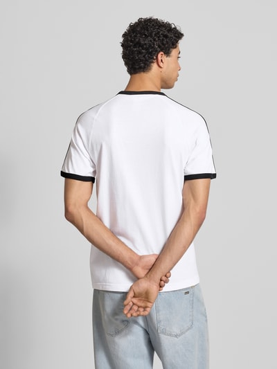 Männermodel trägt T-Shirt mit Label-Stitching von adidas Originals in Weiß mit schwarzen Details, Baumwoll-Mix, Regular Fit, Ganzkörperansicht Rückansicht.