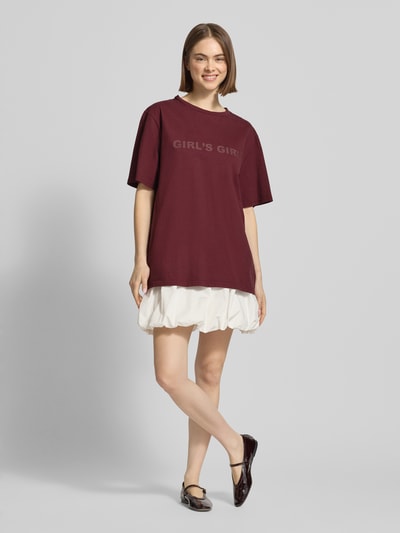 Frauenmodel trägt Oversized T-Shirt mit Statement-Print von OH APRIL in Bordeaux, Reine Baumwolle, Oversized-Fit, Gerippter Rundhalsausschnitt, Rückenlänge bei Größe S 70 cm, Ganzkörperansicht von vorne.