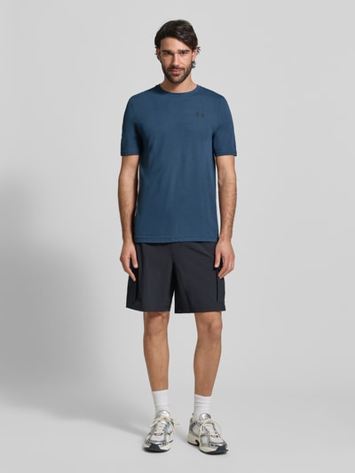 Męski model nosi Slim Fit T-Shirt mit Logo-Print Modell 'Vanish' von Under Armour, kolor niebieski, krój slim fit, motyw logo, okrągły dekolt, tekstura z mikrodziurkami, szerokość w rozmiarze M 40 cm, widok całej sylwetki z przodu.