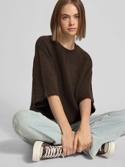 Kobiece modelka nosi brązowy sweter o kroju regular fit z rękawami o dł. 3/4, model 'SIMONI' od ONLY, jasnoniebieskie jeansy, zdjęcie całej sylwetki z przodu, damski sweter od ONLY.