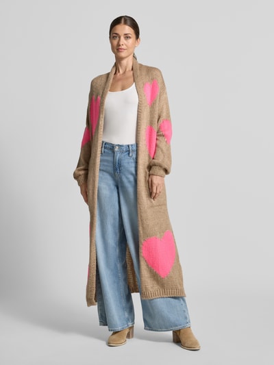 Frauenmodel trägt Strickjacke aus Alpaka-Mix von miss goodlife in Beige mit pinken Herzformen, lockere Passform, Ganzkörperansicht von vorne