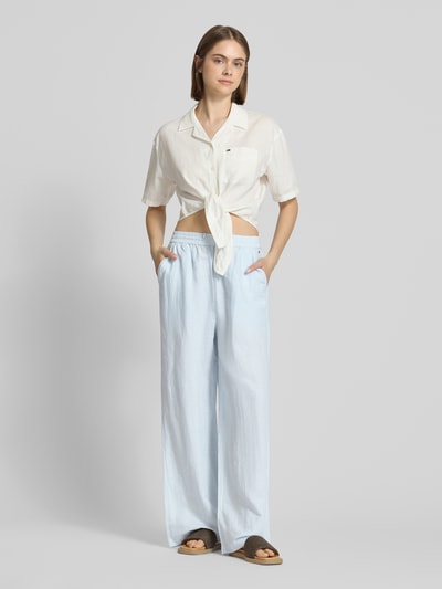 Frauenmodel trägt Weite Hose aus Leinen-Mix mit Tunnelzug von Tommy Jeans in Two-Tone-Optik, Loose-Fit, Logo-Stitching, seitliche Eingrifftaschen und aufgesetzte Gesäßtaschen; hellblaue, strukturierte Oberfläche, Bundabschluss mit Tunnelzug, Ganzkörperansicht von vorne.