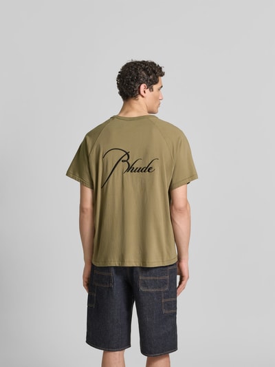 Männermodel trägt Regular Fit T-Shirt aus reiner Baumwolle von RHUDE in Oliv mit Label-Stitching, Raglanärmel, Ganzkörperansicht Rückansicht.