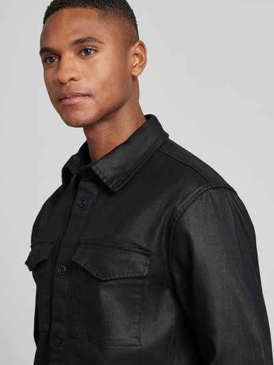 Männermodel trägt Regular Fit Hemdjacke mit Brusttaschen Modell 'THEO' von Guess, schwarzer Baumwoll-Mix, Nahaufnahme Oberkörper.