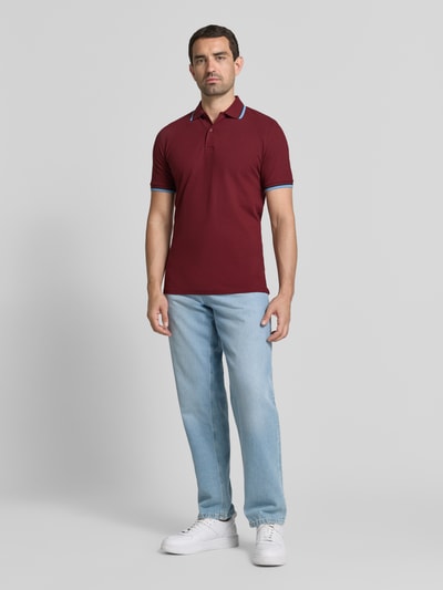 Männermodel trägt Slim Fit Poloshirt aus Baumwoll-Mix Modell 'ATLAS' von Selected Homme in Dunkelrot, Ganzkörperansicht von vorne. Herren Poloshirt.