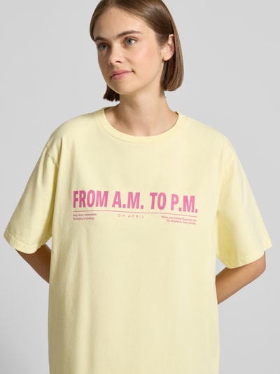 Frauenmodel trägt T-Shirt mit Rundhalsausschnitt Modell 'AM to PM' von OH APRIL in Gelb mit rosa Print aus reiner Baumwolle, Oversized, Nahaufnahme Oberkörper.