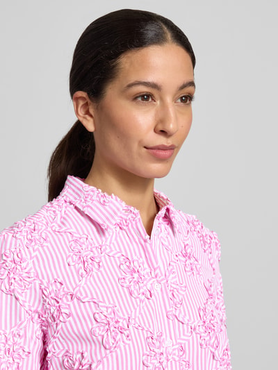 Modelka kobieca nosi HBK Zümdholzstreifen Streifen Bluse mit Blumen Applikationen von Christian Berg Woman, różowe i białe paski, luźny krój, kwiatowe aplikacje, materiał z domieszką bawełny, kołnierzyk koszulowy, zapięcie na guziki, widok na górną część ciała z przodu.